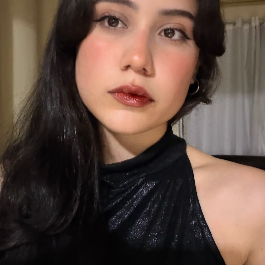 Maria Eduarda, de cabelo preto e blusa de veludo preta, olhando para a câmera.